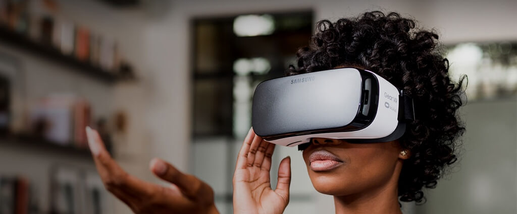 A black woman wearing a VR headset. She has her hand out.
