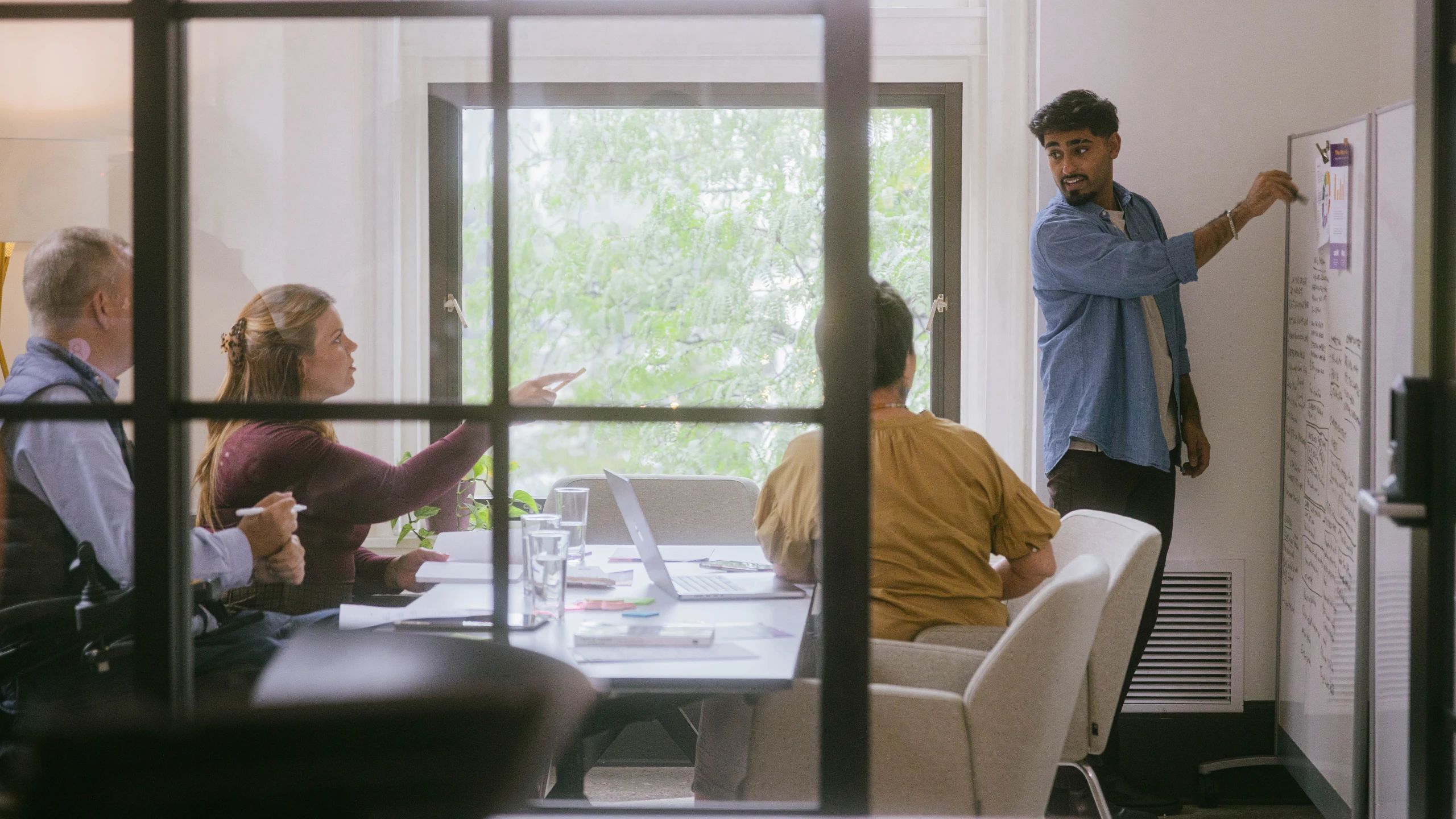 Vervint employees in a conference room working together. One employee is standing at a whiteboard while three others sit at the conference table in deep discussion. 